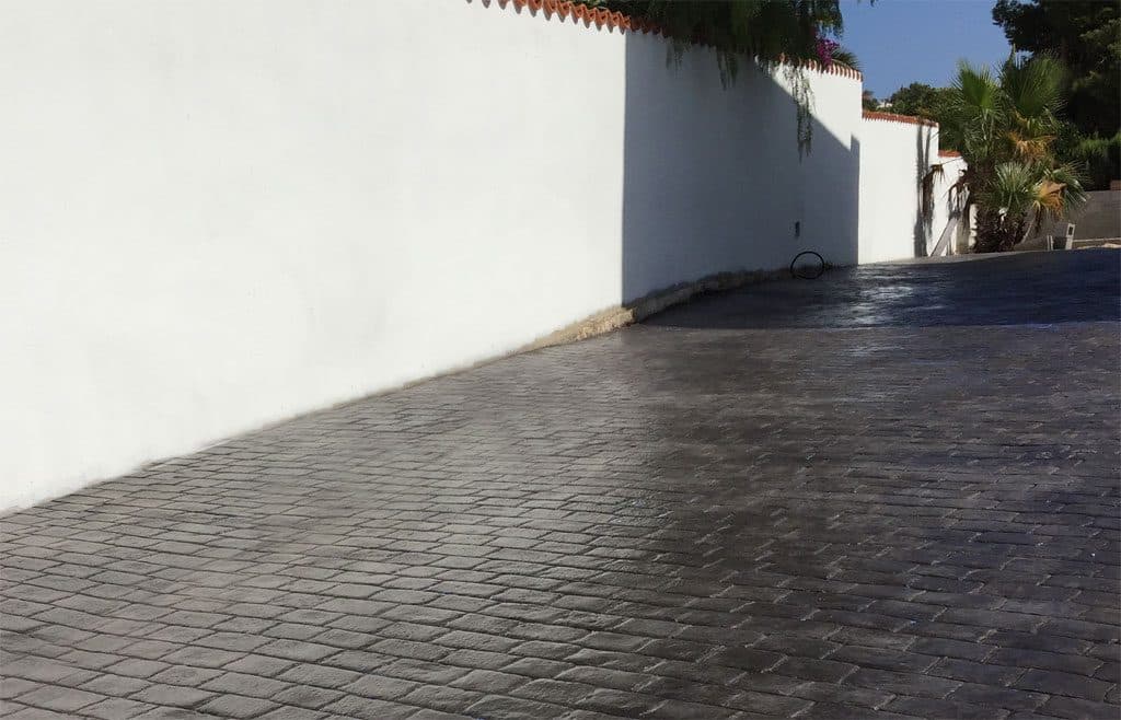 Entrada de vehículos en hormigón impreso gris oscuro junto a la fachada blanca de una vivienda