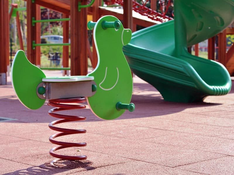 Pavimento continuo de caucho rojo en un parque infantil con balancín y tobogán